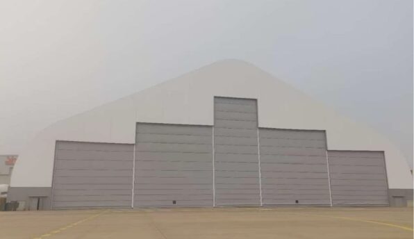 Large white arched aircraft hangar with five gray bay doors on an empty tarmac.