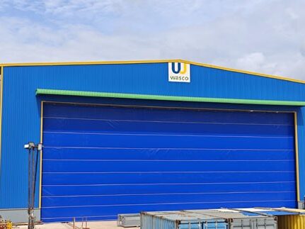 Blue industrial warehouse exterior with a wide cobalt roller door and a Wasco logo above it.