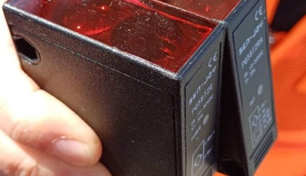 Close-up of a hand holding two black rectangular electrical modules with red translucent tops and labels/CE markings.