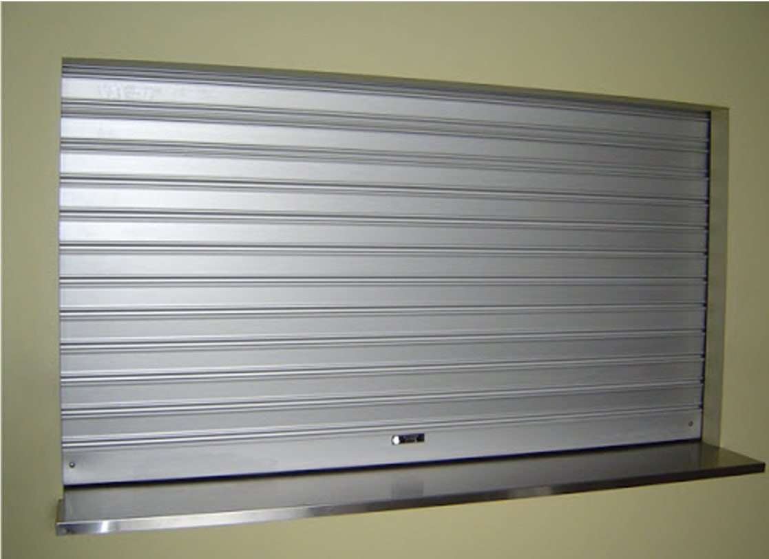 Closed metal rolling shutter covering a wall opening, with a dark countertop below it.